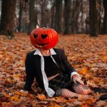 Woman wearing pumpkin sitting on leafs